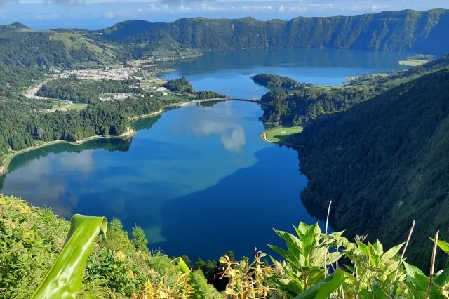 Eine Lagune umgeben von grün bewachsenen Hügeln. Auf der linken Seite ist ein kleines Dorf.
