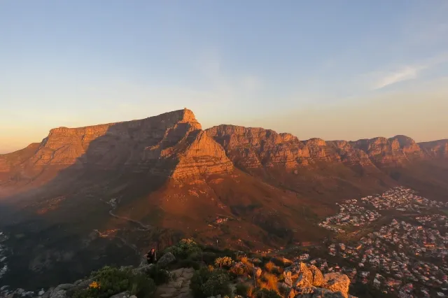 Der Tafelberg ist groß und scheint orange im Abendlicht. Auf der Rechten Seite ist eine Stadt.