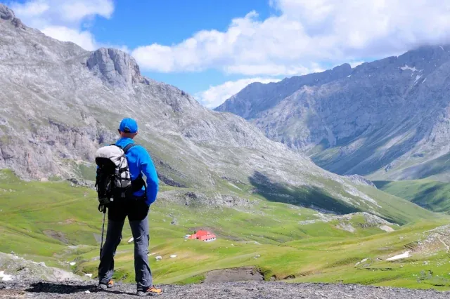 Wanderer mit Rucksack blick auf eine Bergkulisse mit grünen Wiesen und grauen Bergen
