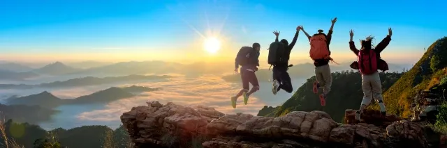 Vier Wanderer springen am Gipfel in die Höhe