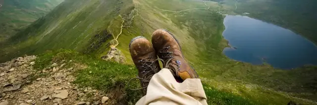 Füße mit Wanderschuhen auf dem Berggipfel mit Blick auf grüne Berglandschaft und blauen See