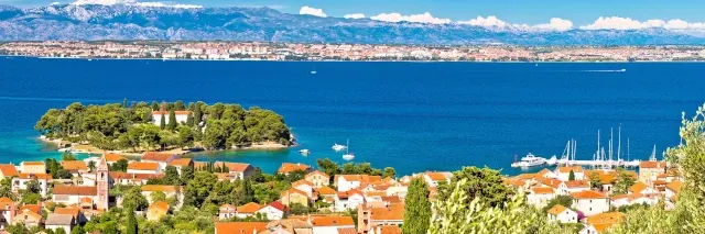 Stadt an der Küste am blauen Meer mit Bergen im Hintergrund unter blauem Himmel