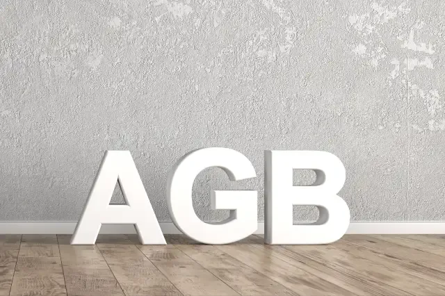 Schriftzug mit AGB steht auf Holzboden vor grauer Wand und weißer Bodenleiste