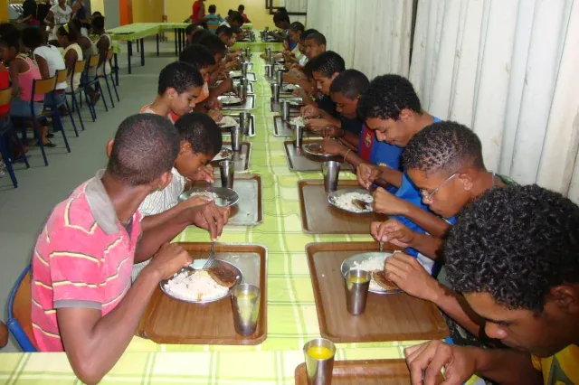 Jungs sitzen entlang eines langen Tisches und essen von Tellern zu Mittag.