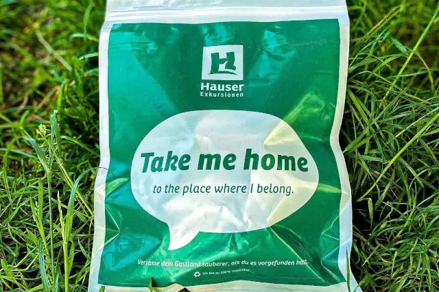 Auf dem Gras liegt ein Grün-weißer Beutel mit dem Firmenlogo und dem Begriff take-me-home