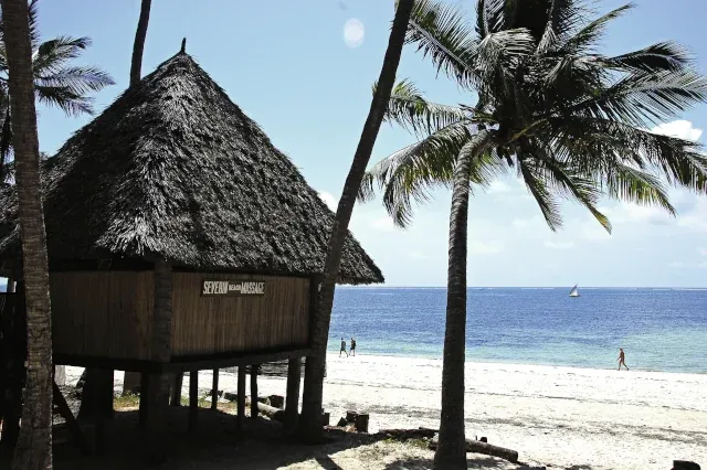 Eine runde Hütte auf Stelzen steht an einem Strand. Neben der Hütte steht eine Palme und im Hintergrund ist das Meer zu sehen.
