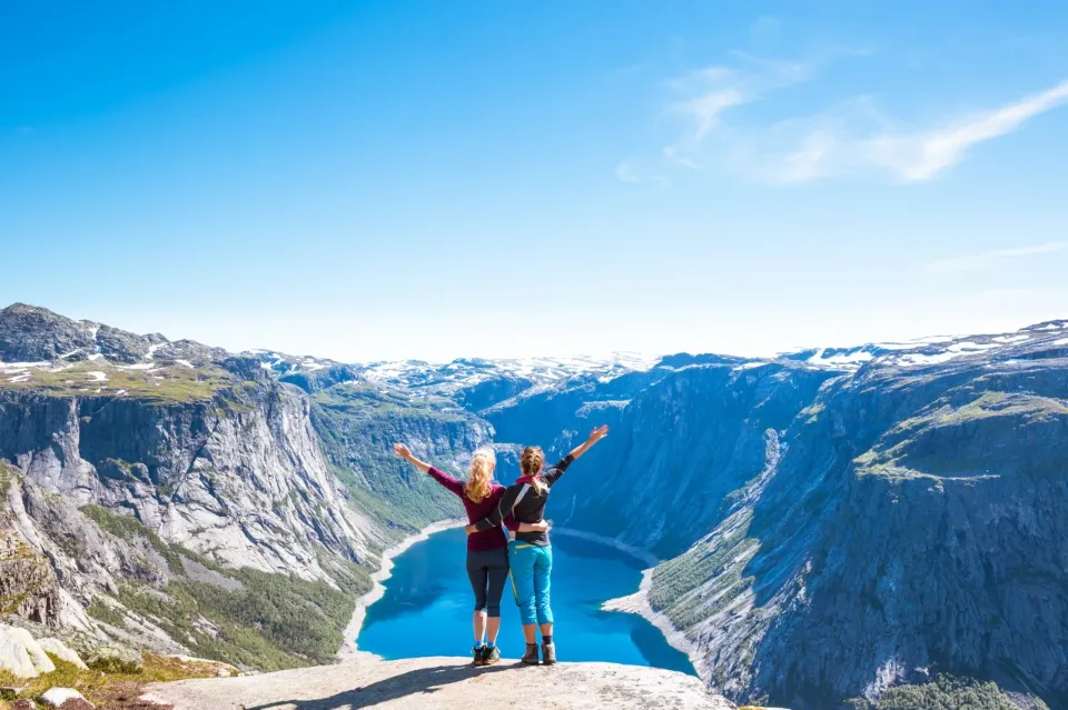 Zwei Frauen stehen an der Klippen und blicken auf Berge und einen blauen See