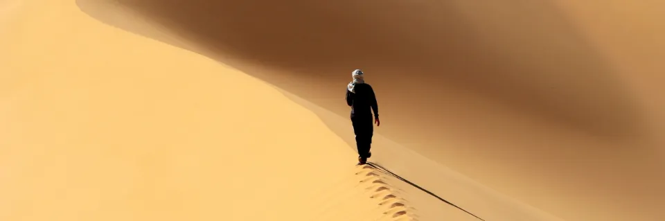 Wanderer läuft auf einer Sanddüne mit Fußspuren hinter ihm im Sand