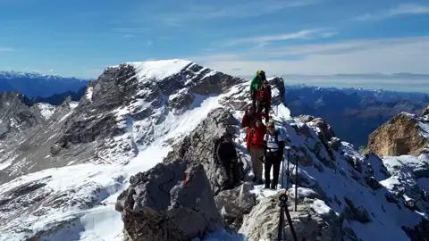 Wandergruppe auf einem verschneiten Berggrat mit Blick auf die umliegenden Berge und Gletscher.