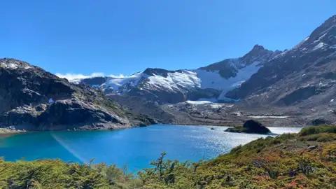 Türkisfarbener Bergsee mit schneebedeckten Bergen und Gletschern im Hintergrund.