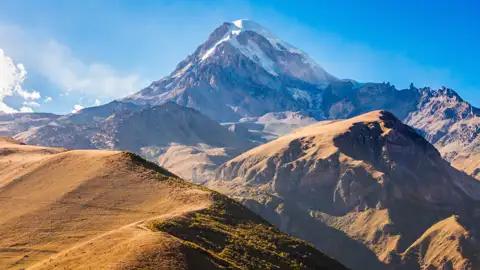 Die Swetizchoweli-Kathedrale in Mzcheta, Georgien. Die alten Steinmauern der Kathedrale erheben sich hinter einem Verkaufsstand mit bunten Tüchern.