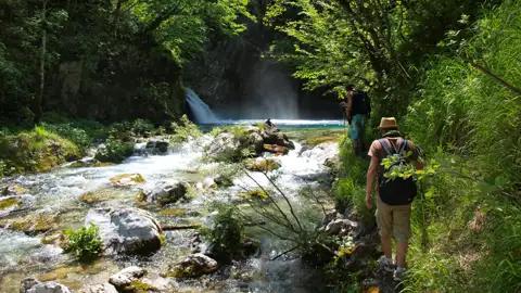 Wanderer auf einem Flussweg in der Nähe eines Wasserfalls.