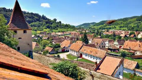 Blick auf ein traditionelles Dorf mit roten Ziegeldächern und einem Kirchturm.