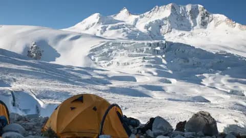 Zeltlager inmitten einer verschneiten Berglandschaft mit Gletscher im Hintergrund.