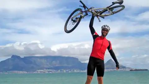 Erfolgreicher Abschluss einer Radtour: Radfahrer mit erhobenem Fahrrad vor dem Tafelberg.