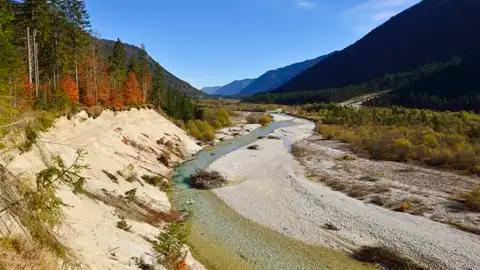 Flusslandschaft im Herbst mit bunten Bäumen und sandigem Ufer.