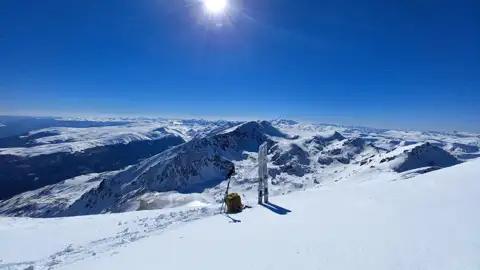 Skiausrüstung auf einem sonnigen Berggipfel mit Panoramablick auf die verschneite Bergkette.
