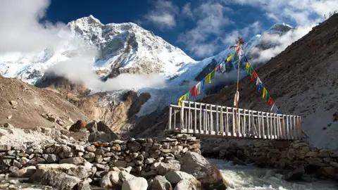 Holzbrücke mit Gebetsfahnen im Himalaya Gebirge.