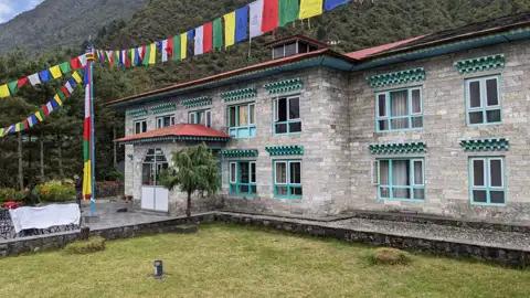 Gebetsfahnen wehen vor einem Steinhaus, das möglicherweise als Unterkunft während der Reise dient.