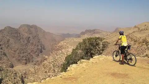 Mountainbiker mit Helm und Fahrrad am Rande einer Klippe mit Blick auf eine Wüstenschlucht.