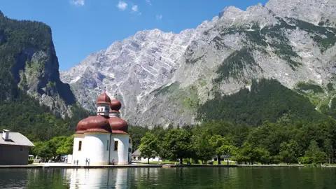 Blick auf die St. Bartholomä Kirche mit dem Königssee und den Berchtesgadener Alpen im Hintergrund.