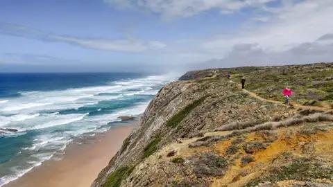 Wanderer auf einem Pfad entlang der Küste mit Blick auf den Ozean und die Wellen.