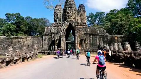 Kambodscha Radreise. Radfahrer auf einer Reise durch Angkor Thom, passieren das Südtor mit den charakteristischen Gesichtern und den steinernen Wächterfiguren.