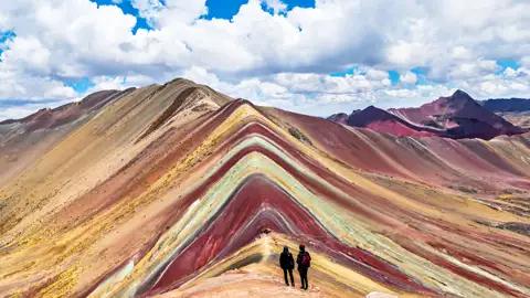 Zwei Wanderer auf dem Vinicunca, auch bekannt als Regenbogenberg, bewundern die vielfarbigen Gesteinsschichten.