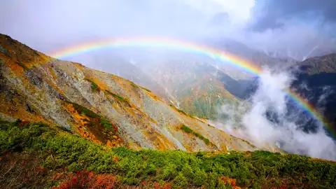Regenbogen über herbstlichen Bergen.