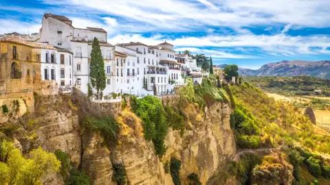 Weiße Häuser einer Stadt, die dramatisch am Rande einer hohen Klippe liegen.