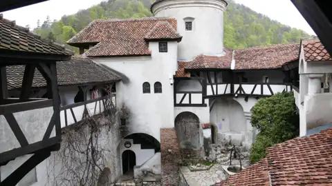 Blick auf den Innenhof der Burg mit seinen architektonischen Details wie den weißen Wänden, dem Fachwerk und den roten Ziegeldächern. Ein Brunnen befindet sich in der Mitte des Hofes.