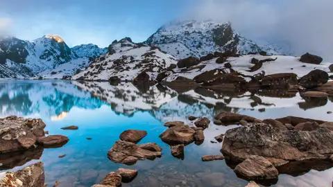 Ruhiger Bergsee mit Spiegelung der umliegenden schneebedeckten Berglandschaft.