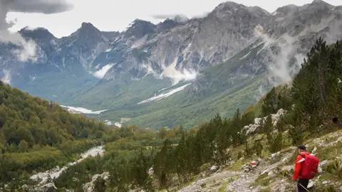 Wanderer auf einem Bergpfad mit Blick auf ein Tal und die umliegenden Berge.