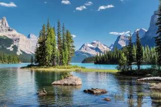 Blick auf einen Gebirgssee, der von felsigen Bergen umgeben ist. Auf dem See sind kleine Inseln zu sehen auf denen vereinzelt Nadelbäume wachsen.
