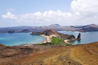Eine felsige Landschaft. In der Mitte ist blaues Wasser mit einer Landzunge mit zwei Stränden.