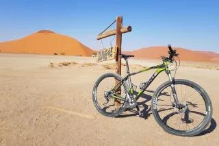 Ein Mountainbike Fahrrad lehnt an einem Schild, auf dem "Dune 45" steht. Dahinter ist eine große Düne.