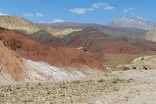 Mehrere bunt gefärbte Hügel und Berge in einer steinigen Landschaft. Der Himmel ist blau.