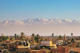 Eine Stadt mit rötlich braunen Gebäuden. Dahinter ist ein hohes, schneebedecktes Gebirge.