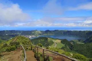 Ein Wanderweg führt zu einem Aussichtspunkt, von dem man eine Lagune und die grüne Landschaft sieht.