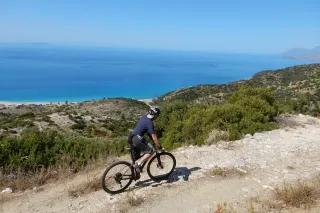 Radfahrer mit Mountainbike fährt über einen Weg an der Küste mit Blick auf das blaue Meer