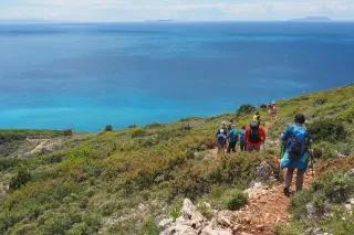 Gruppe von Wanderern laufen an der Küste bergab in Richtung Strand mit Blick auf das blaue Meer