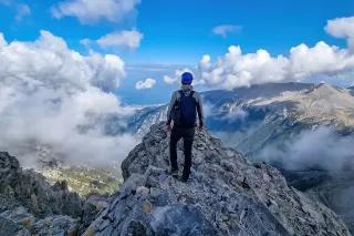 Mann mit Rucksack steht auf einem wolkenverhangenen Berggipfel und blickt in die Ferne