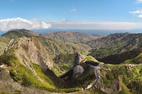 Ein zerklüftetes Bergpanorama. Die Berge sind grün bewachsen. In der Ferne ist das Meer.