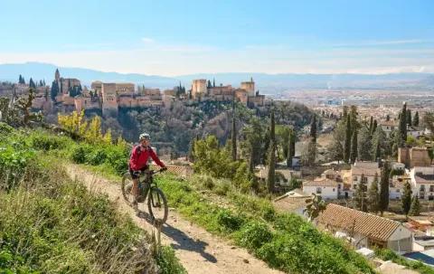 Eine Frau radelt mit ihrem E-Bike auf einer Schotterpiste. Im Hintergrund sieht man eine Stadt und eine Burg.