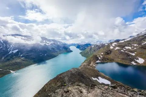 Blick auf eine Fjordlandschaft von oben. Rechts und links neben den Flüssen sind hügelige Landschaften mit Altschneefeldern zu sehen.