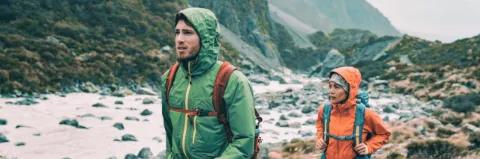 Ein Mann und eine Frau mit Rucksäcken und Regenkleidung in einer Bergumgebung