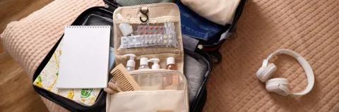 Ein offener Reisekoffer mit Reiseapotheke liegt auf einem Bett