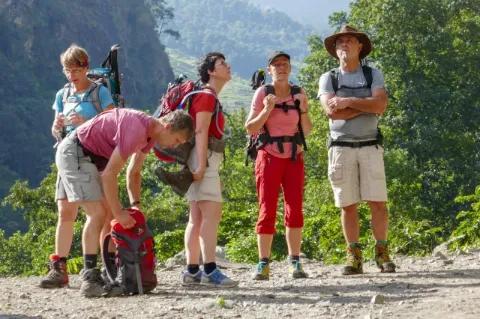 Eine Gruppe von fünf Wanderern steht auf einem Platteau in einer Berglandschaft. Ein Wanderer kramt in seinem Rucksack, der auf dem Boden steht.