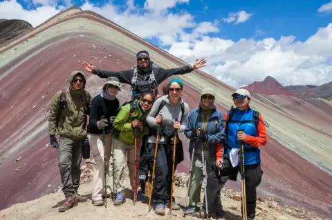 Eine Gruppe Wanderer steht vor den Regenbogenbergen in Peru und grinst in die Kamera.