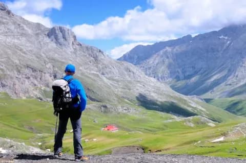 Wanderer mit Rucksack blick auf eine Bergkulisse mit grünen Wiesen und grauen Bergen